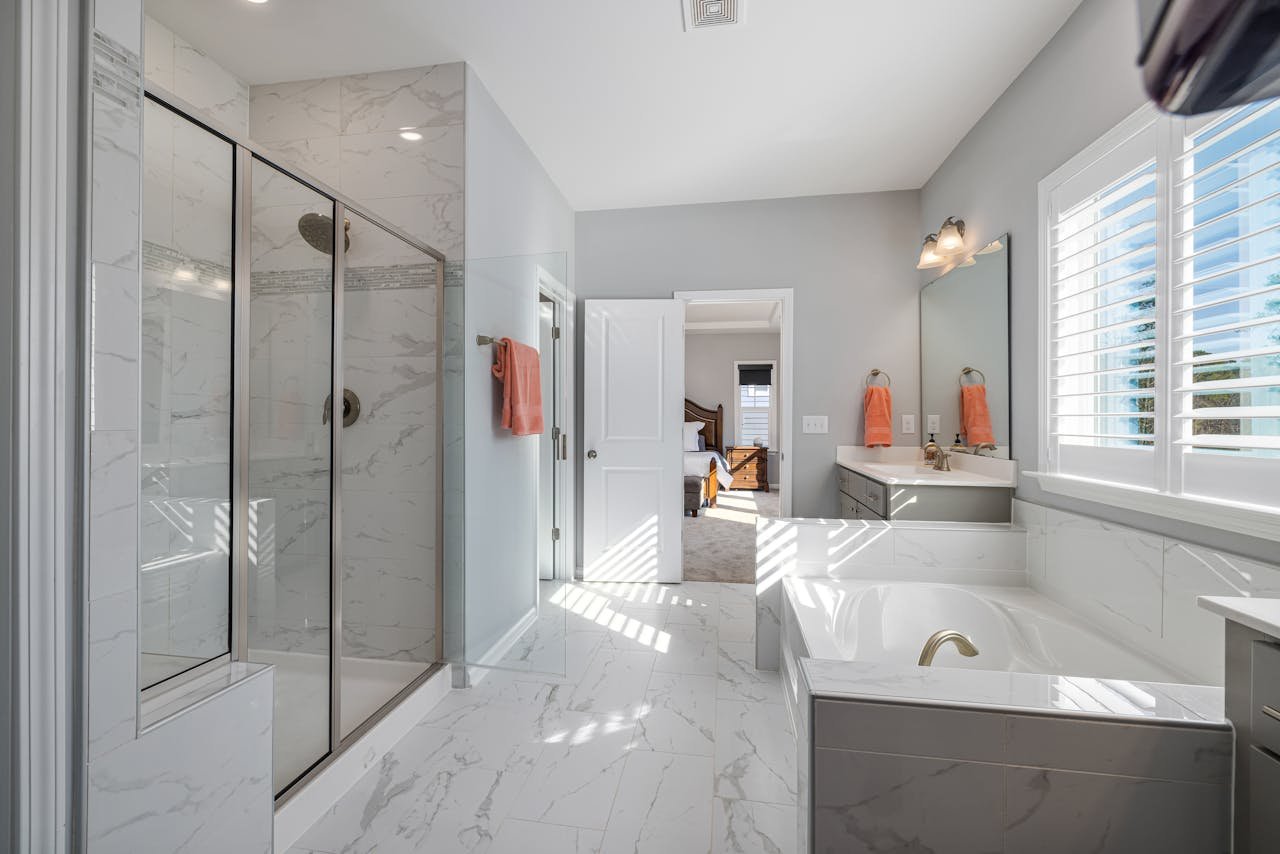 A spacious, modern bathroom featuring marble surfaces, a glass shower, and ample natural lighting.