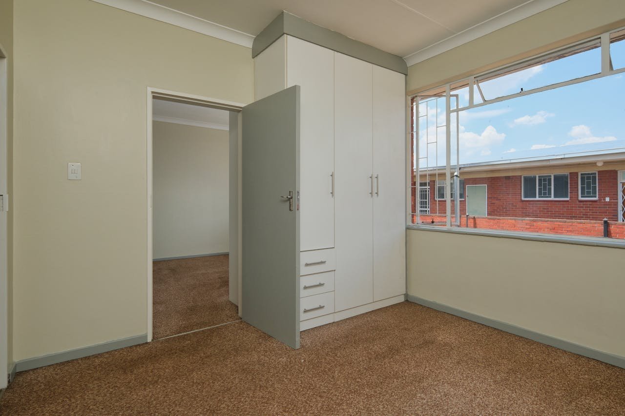 Clean, spacious empty room with carpet and large window, perfect for real estate listings or interior design inspiration.