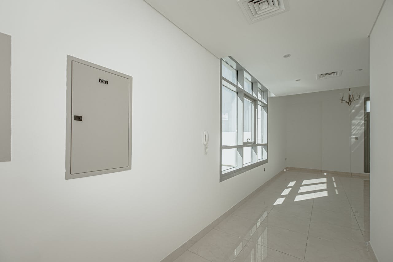 A clean, minimalistic empty corridor with natural light streaming through large windows.